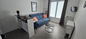 Ein kompakter Wohnraum mit Küchenzeile, einer Couch mit Kissen, einem kleinen runden Tisch und einem an der Wand befestigten Fernseher.