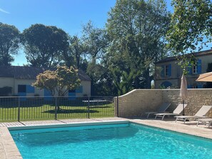 A swimming pool with a stone wall and lounge chairs.