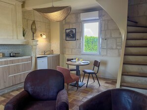 A compact kitchen with a dining area, stone walls, and a window with a view.