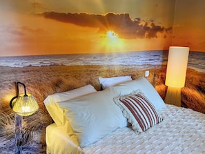 A bed with white linens and a striped pillow, a lamp, and a wall mural of a sunset over the ocean. - Mas Dou Rose, farmhouse with swimming pool near Alpilles (Arles)