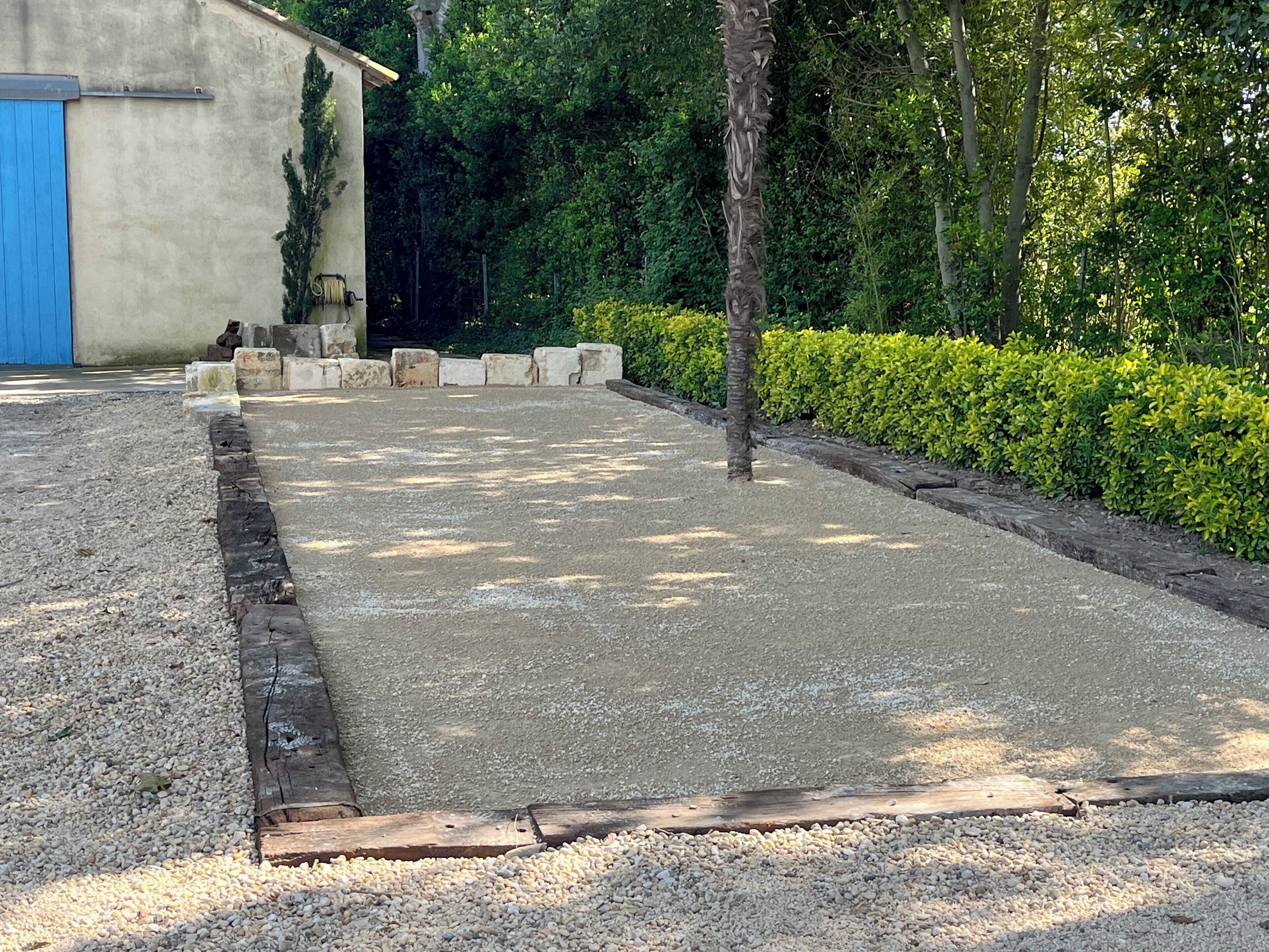 Une zone pavée bordée de béton, entourée de verdure et d’un bâtiment bleu.