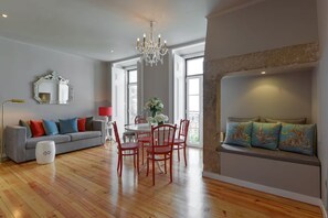 Ein modernes Wohnzimmer mit einem grauen Sofa, roten Sesseln, einer Kristallleuchtre und einem Kamin aus Stein.