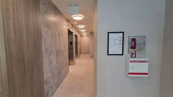 A hallway with marble walls, a fire safety plan sign, a smoke detector, and a fire alarm pull station.