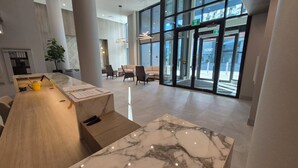 A modern hotel lobby with a reception desk, seating area, and large windows offering views of the street. - Kelowna Aqua Waterfront Rental (Kelowna)