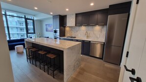A modern kitchen with a marble countertop, stainless steel appliances, and a bar area. - Kelowna Aqua Waterfront Rental (Kelowna)