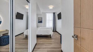 Una habitación de hotel moderna con una cama, un escritorio, una silla, un televisor y un espejo.