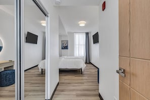A modern hotel room with a bed, a desk, a chair, a TV, and a mirror. - Downtown Indy Grand Flat 2,800 Sqft- Flat 9 (Indianapolis)