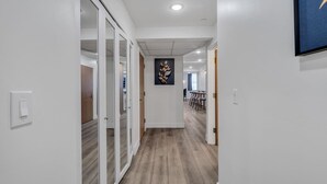 Un pasillo con piso de madera, paredes blancas y una puerta que da a un comedor con sillas y una mesa.