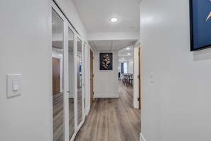 A hallway with a wooden floor, white walls, and a door leading to a dining area with chairs and a table. - Downtown Indy Grand Flat 2,800 Sqft- Flat 9 (Indianapolis)