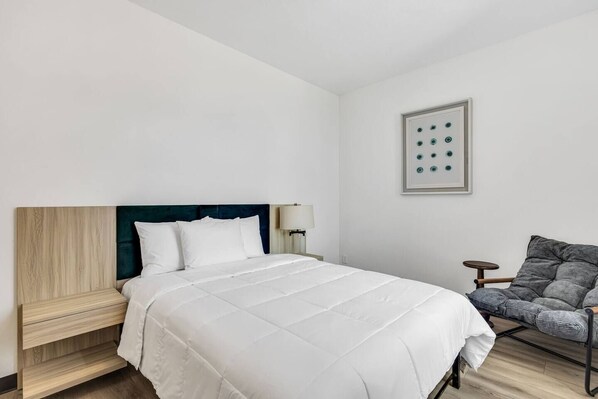 A modern hotel room with a bed, bedside table, chair, and a wall-mounted lamp. - Downtown Indy Grand Flat 2,800 Sqft- Flat 5 (Indianapolis)