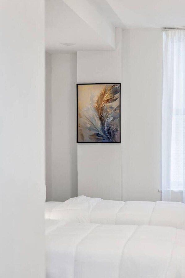 A bedroom with a bed, a framed abstract painting on the wall, and a window with curtains. - Downtown Indy Grand Flat 2,800 Sqft- Flat 5 (Indianapolis)