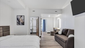 Hotellihuone, jossa on sänky, sohva, peili ja ovi, joka johtaa kylpyhuoneeseen.