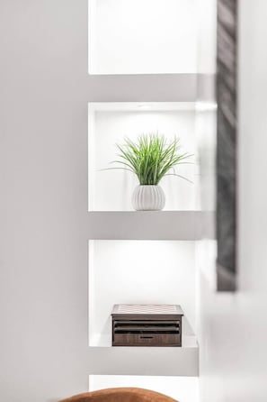 Ein modernes Interieur mit einer weißen Wand, einem Regal mit einer Topfpflanze und einem hölzernen Gegenstand.