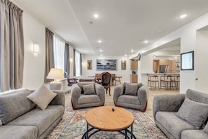 Ein modernes Wohnzimmer mit grauen Sofas, einem runden Holztisch und einem Essbereich mit Holzstühlen.