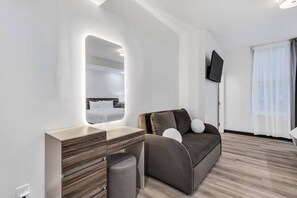 Ein modernes Hotelzimmer mit einem Holztischchen, einer Couch mit Kissen, einem Flachbildfernseher und einem großen Spiegel.