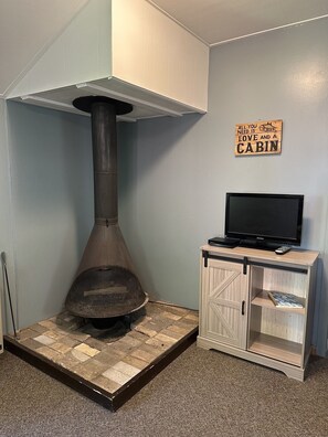 A room with a wood-burning stove, a television on a cabinet, and a sign on the wall.