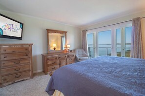 A bedroom with a bed, dresser, mirror, and a view of the ocean. - Sunset Corner ~ Surrounding river views (Folly Beach)