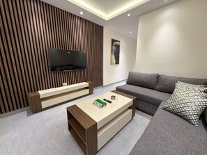 Una sala de estar moderna con televisor de pantalla plana, un sofá gris, una mesa de centro y un cojín estampado.