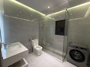 Un baño moderno con ducha de vidrio, inodoro, lavamanos y lavadora.