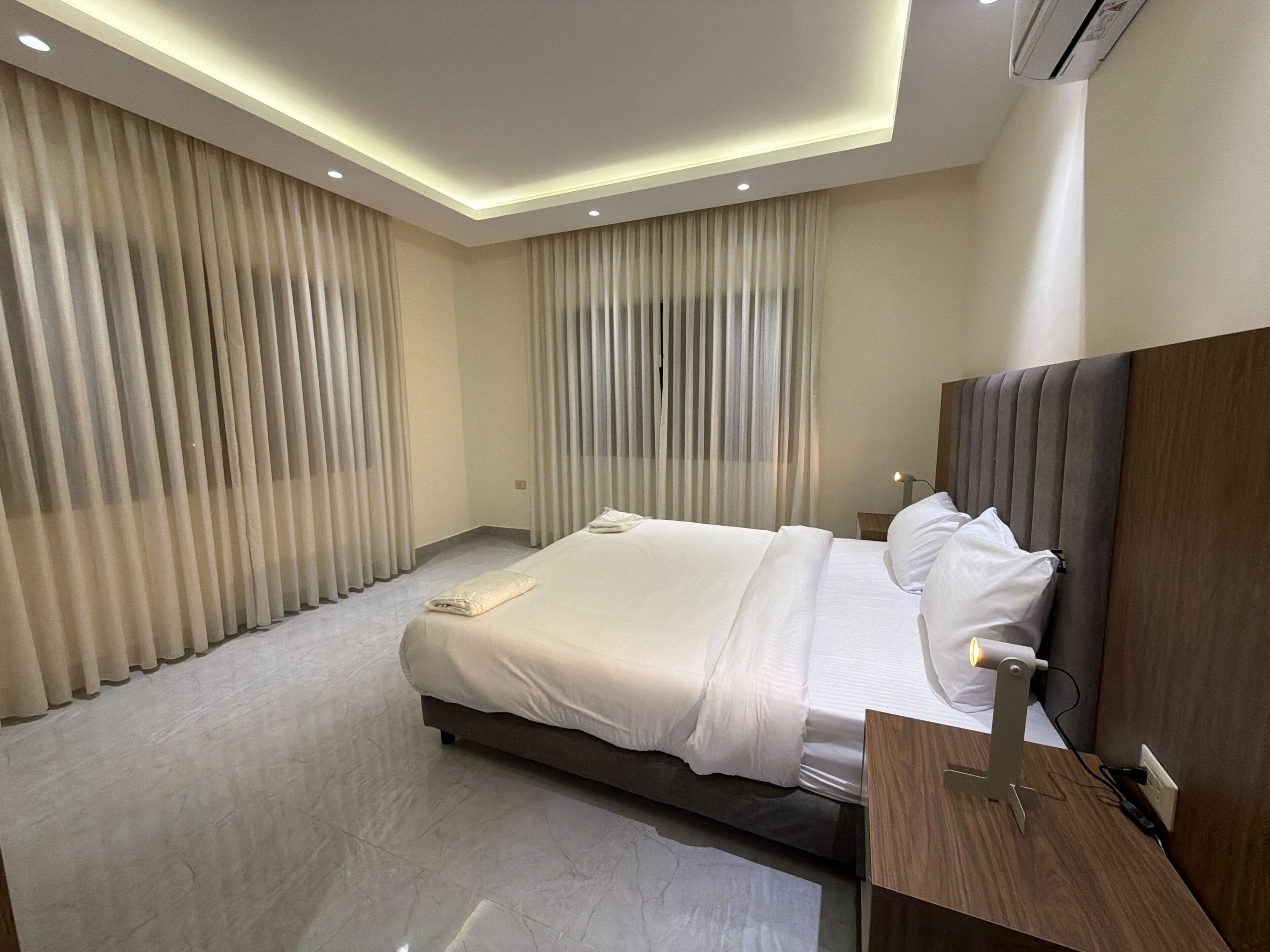 Una habitación de hotel moderna con una cama grande, un cabecero de madera y una mesita de noche con una lámpara.
