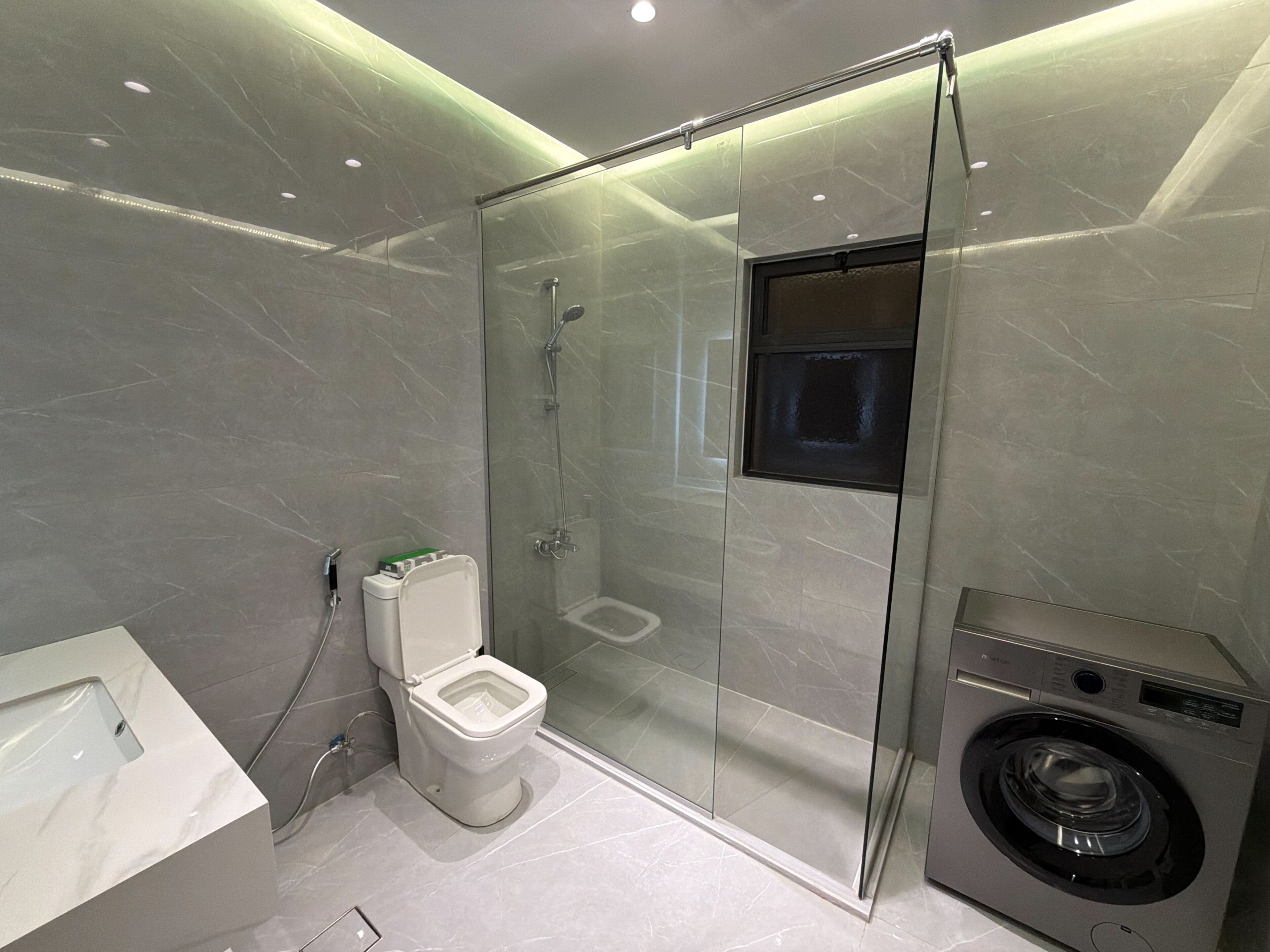Une salle de bain moderne dotée d’une douche à parois de verre, de toilettes et d’un lave-linge.