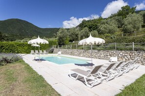Ein Poolbereich mit Liegestühlen und Sonnenschirmen, umgeben von Steinmauern und viel Grün.