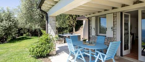 An outdoor patio with a table and chairs, a stone wall, and a view of the sea.