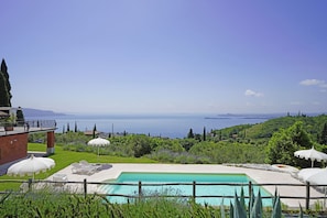 A pool with a view of the sea, surrounded by greenery and white umbrellas. - Ca Pietra By Garda FeWo a Toscolano Maderno (Toscolano-Maderno)