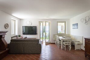 Ein Wohnzimmer mit Sofa, Fernseher, Esstisch, Stühlen und Blick durch eine Glastür.