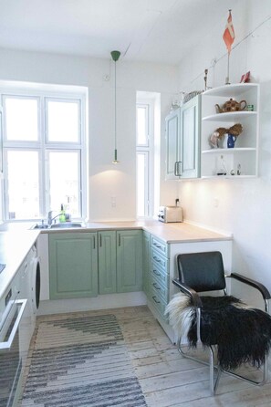 Une cuisine avec des meubles de couleur verte, un évier, une chaise et une fenêtre.