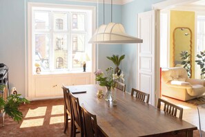 A dining area with a wooden table, chairs, a vase with flowers, a large window, and a chair with a cushion. - Magnificent Copenhagen home with artistic charm (Frederiksberg)