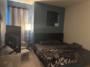 A hotel room with a bed, a desk with a computer, a lamp, and a window.