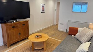 A living room with a TV, wooden cabinet, round coffee table, and a sofa with cushions. - Enjoyable 3-bedroom apartment in charming Hampton Wick neighborhood (Hampton Wick)