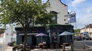 A building with a white facade and a curved top, a tree in front, outdoor seating, and a signboard. - Enjoyable 3-bedroom apartment in charming Hampton Wick neighborhood (Hampton Wick)