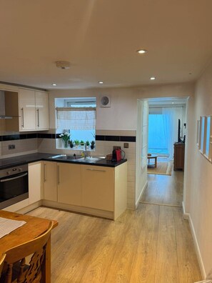 A modern kitchen with a central island, built-in oven, and a dining area with a wooden table and chairs. - Enjoyable 3-bedroom apartment in charming Hampton Wick neighborhood (Hampton Wick)