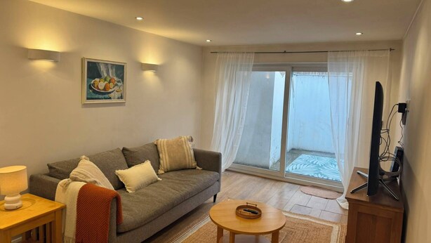A living room with a sofa, a small table, a TV, and a sliding glass door leading to an outdoor area. - Enjoyable 3-bedroom apartment in charming Hampton Wick neighborhood (Hampton Wick)