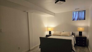 Et soveværelse med en seng, to sengeborde med lamper, et vindue med gardiner og en loftlampe.