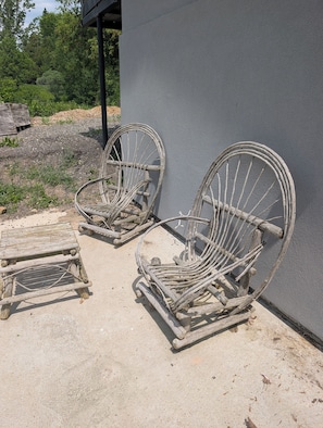 Two rustic metal chairs with wooden frames, positioned on a concrete surface against a grey wall.