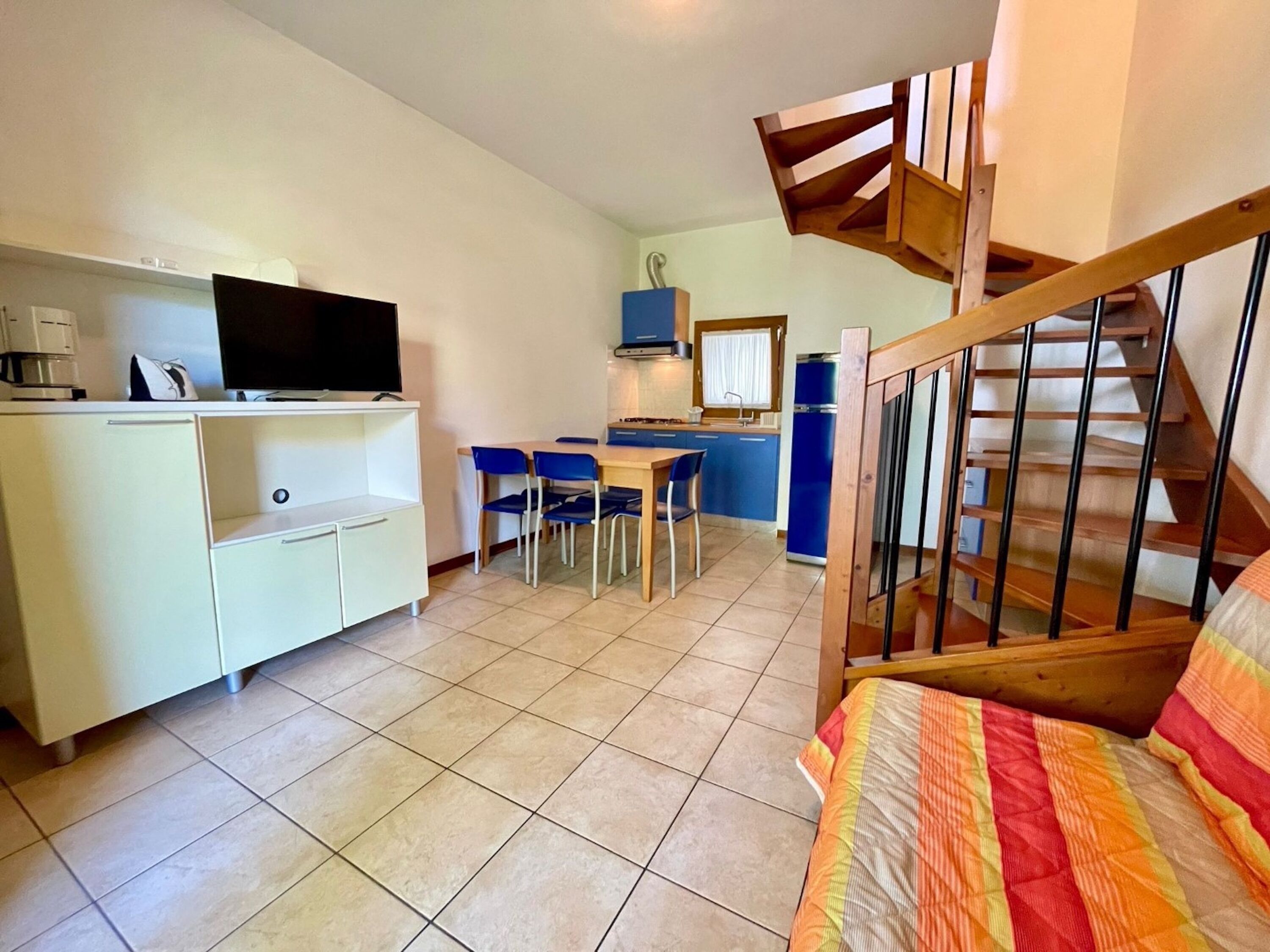 Habitació senzilla amb llit, petita cuina, zona de dinar i escala.