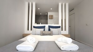Ein modernes Hotelzimmer mit einem großen Bett, zwei Nachttischen, einem Spiegel und einem durch eine Glasscheibe einsehbaren Badezimmer.