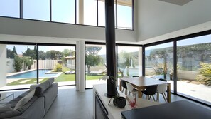 Ein modernes Interieur mit Essbereich, einer Couch und großen Fenstern mit Blick auf Pool und Garten.