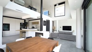 A modern kitchen with a dining area, a living room with a sofa, and a TV mounted on the wall. - Villa d'Exception sur la Presqu'île de Cassis - Heated pool & calanques view (Cassis)