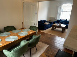 A dining area with a wooden table and green chairs, a living room with a blue sofa and a coffee table, and a white door. - Charming Victorian Townhouse & Garden (London)