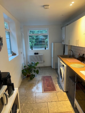 A compact kitchen with a washing machine, a radiator, and a window with plants. - Charming Victorian Townhouse & Garden (London)