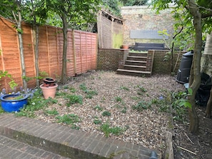 A backyard with a brick wall, a wooden fence, steps leading to a higher level, and a blue pot.