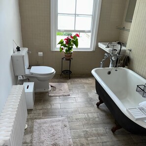 A bathroom with a toilet, bidet, bathtub, radiator, and a window with a plant. - Charming Victorian Townhouse & Garden (London)