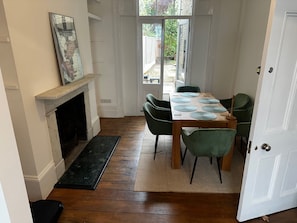 A dining area with a wooden table, green chairs, a fireplace, and a view through a glass door.