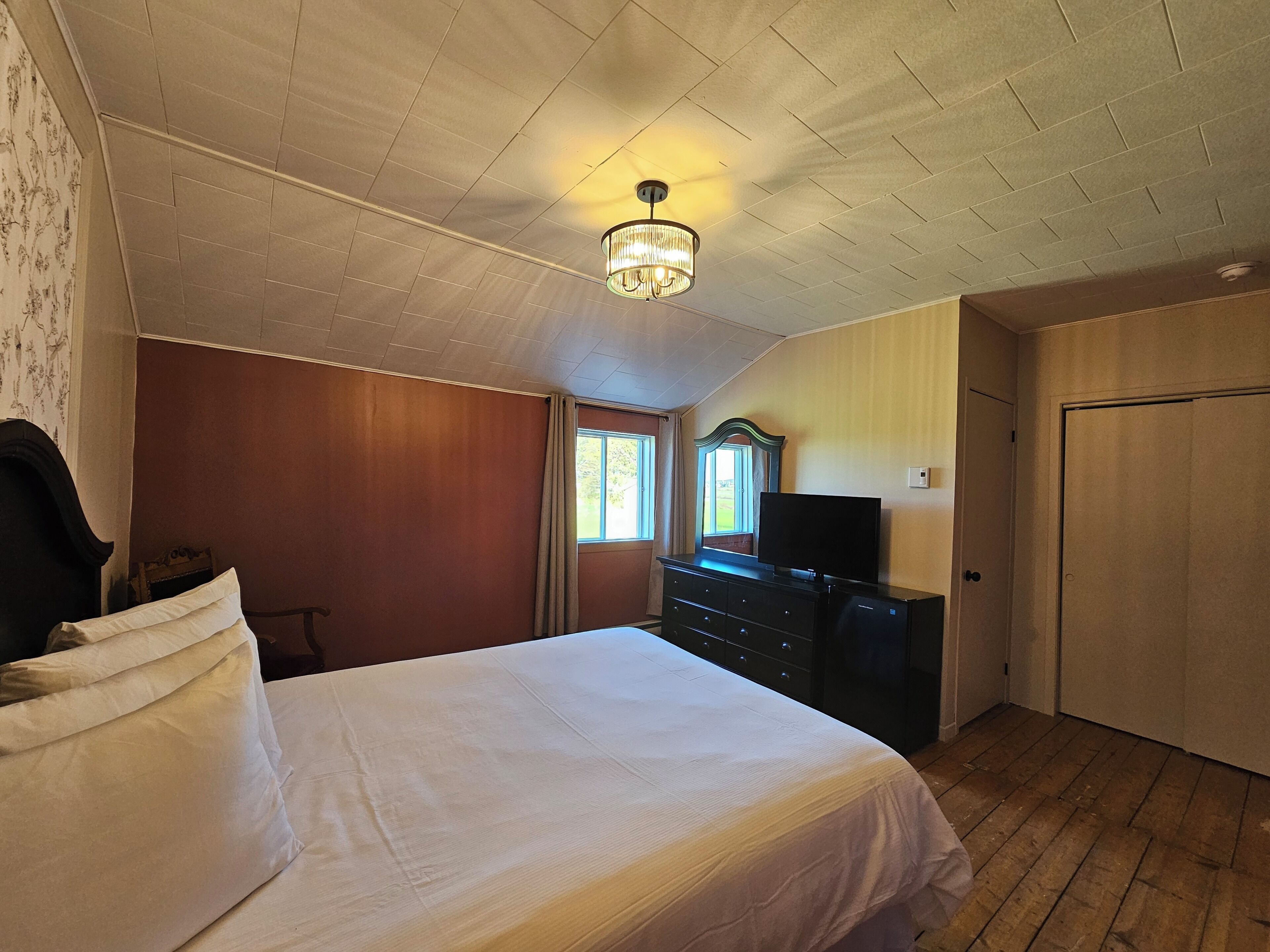 Quarto com cama, cômoda, televisão e porta.