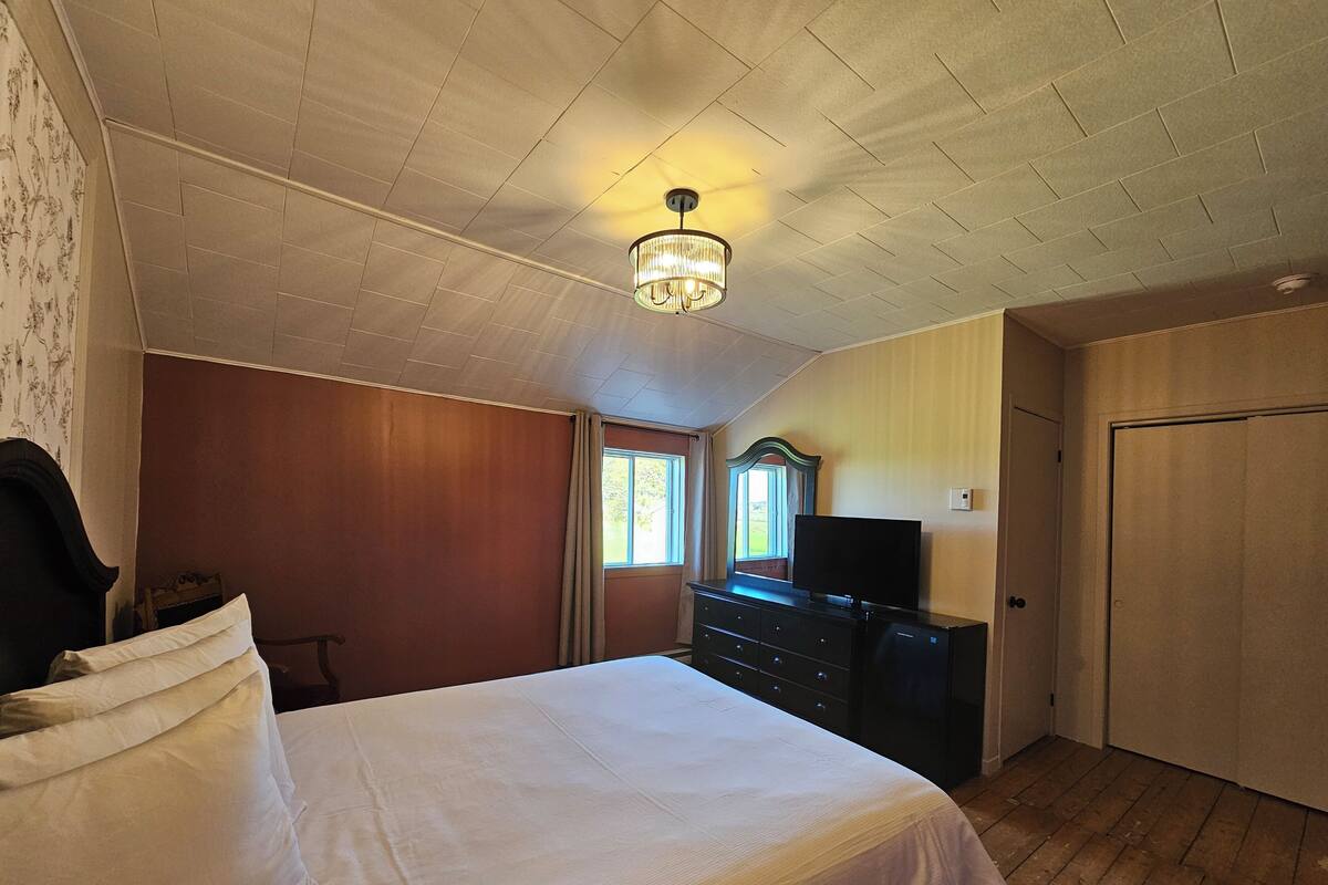 A bedroom with a bed, dresser, TV, and a door.