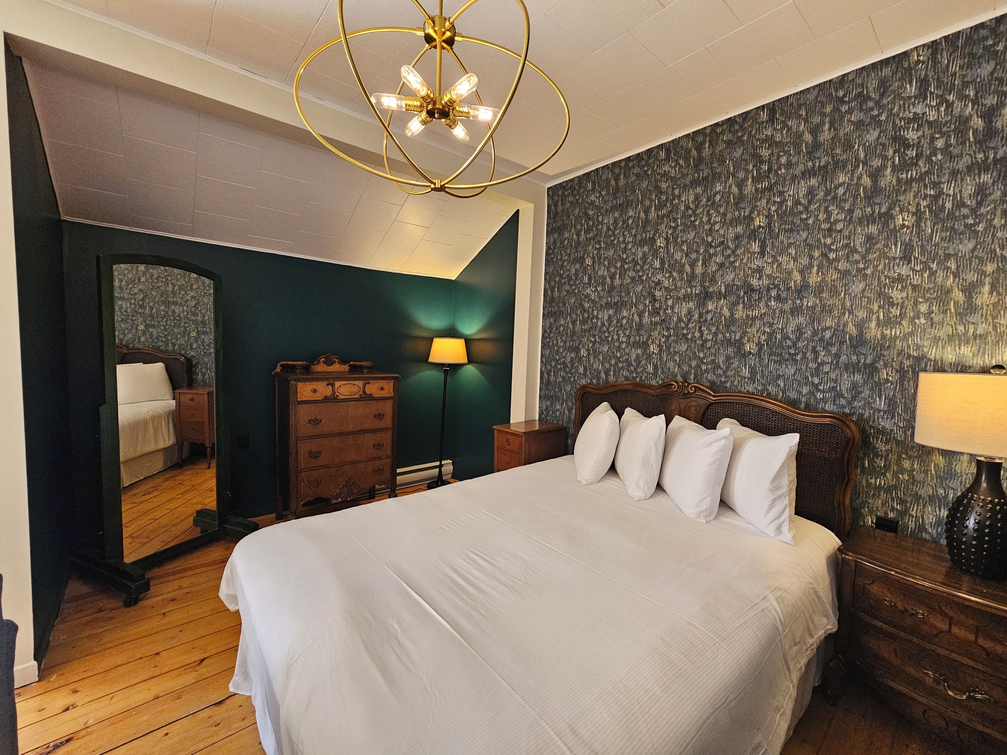Quarto com uma cama grande, cômoda, mesa de cabeceira, abajur e espelho.